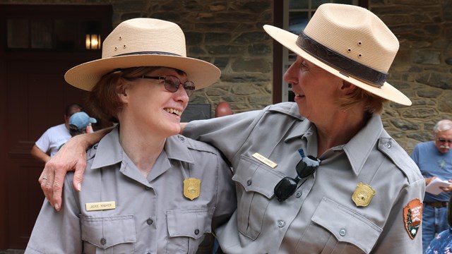 Two rangers wearing the NPS uniform embrace for a photograph. 