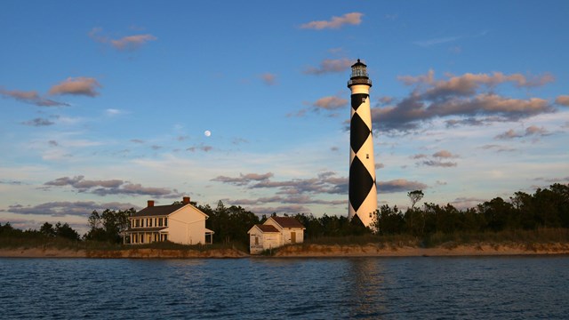 Lighthouse and keeper's quarters with blue sky and water in foreground