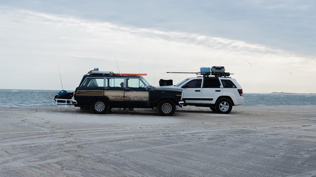 Two cars parks on sand during dusk. 