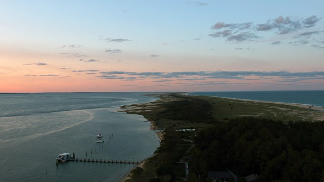 A aerial view of the dock at the Lighthouse. The sun is setting. The land is on the right