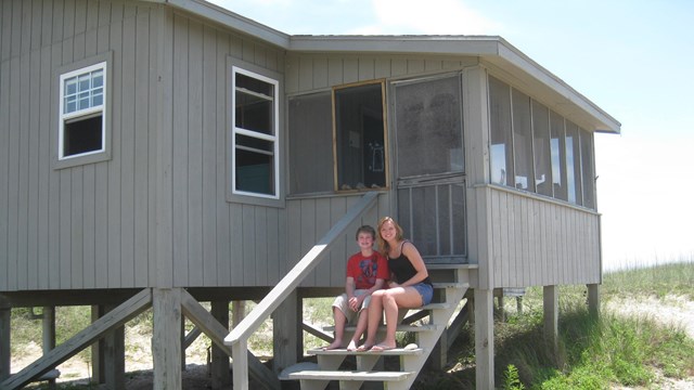 2 people sit on the steps leading to an elevated cabin