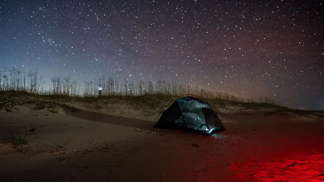 A tent on the beach with star filled skies. 