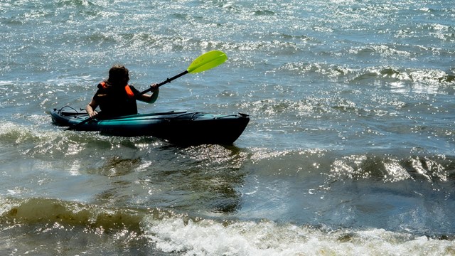 A person kayaks in water. 