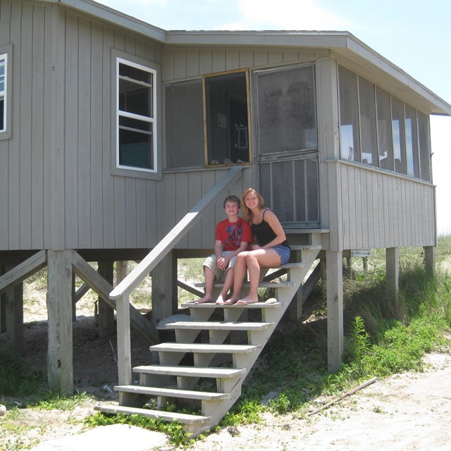 2 people sit on the steps leading to an elevated cabin