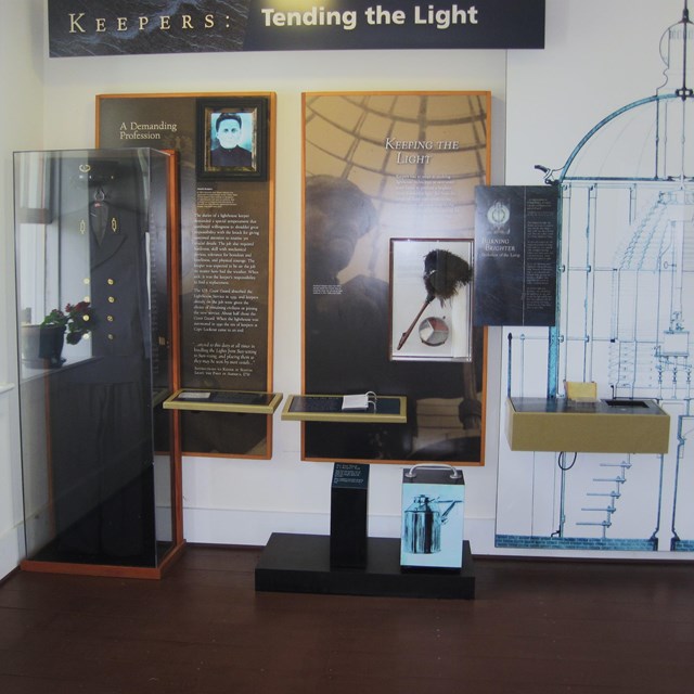 Keeper's uniform, Fresnel Lens drawing, and other displays on a white wall. 