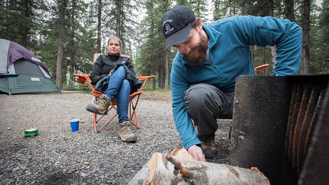 A man adjusts firewood in a camping fire pit