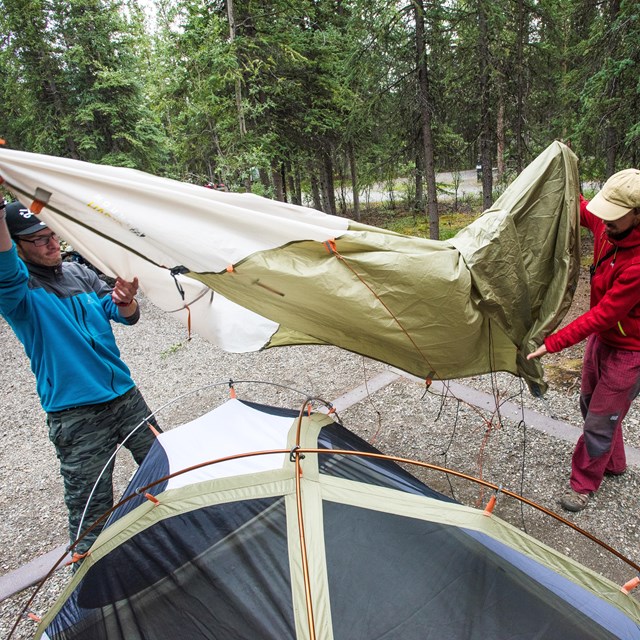 Two men remove a tent green fly from their tent