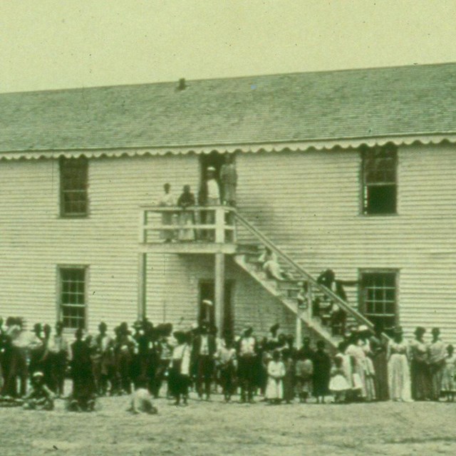 Historic photograph of three teachers with a large group of African American Refugee children.