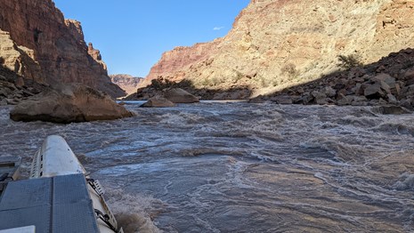 White boat going through rapids in a canyon