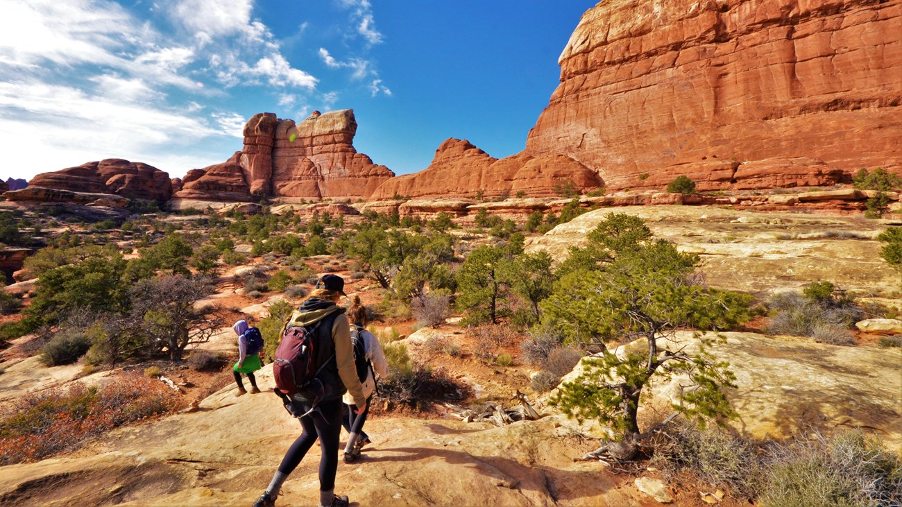 three hikers on smooth sandstone in front of looming red cliffs