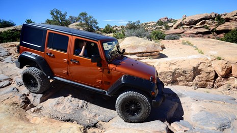 an orange Jeep driving over a steep, rocky surface