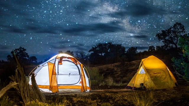 Two tents lit up at night with the night sky in the background.