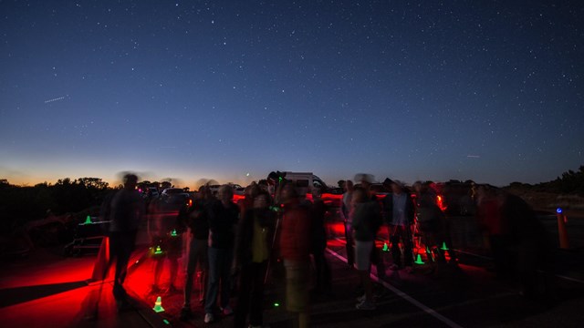 Silhouetted people standing around with red and green lights under a starry sky