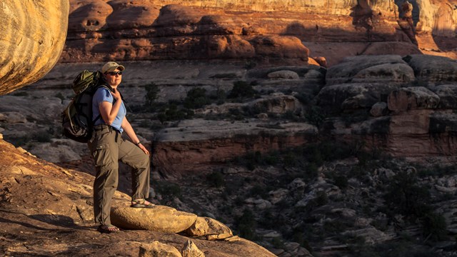 a backpacker stands on a ledge overlooking a canyon