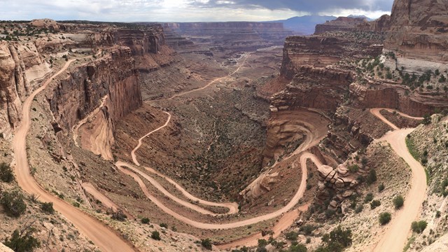 A switchback trail leading up a cliff. Grey clouds hand in the sky above.