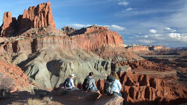 Three hikers sitting on rocks overlooking a vast landscape of rock and cliffs.