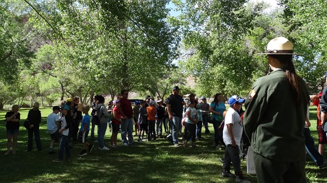 A ranger stands in a grassy field with a group of kids