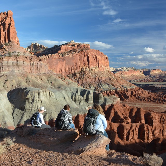 Three hikers sitting on rocks overlooking a vast landscape of rock and cliffs.