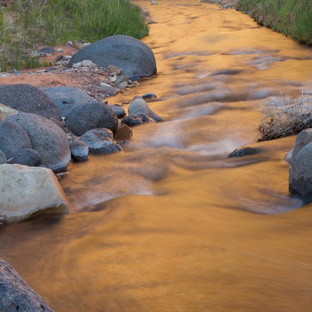A calm stream with rounded black boulders.