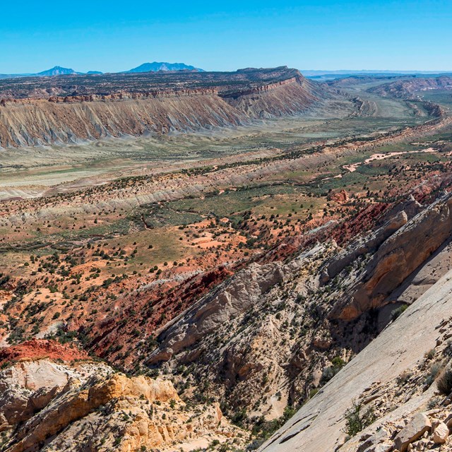 A sweeping view from a ridge top of multicolored bands of rock stretching out for miles.