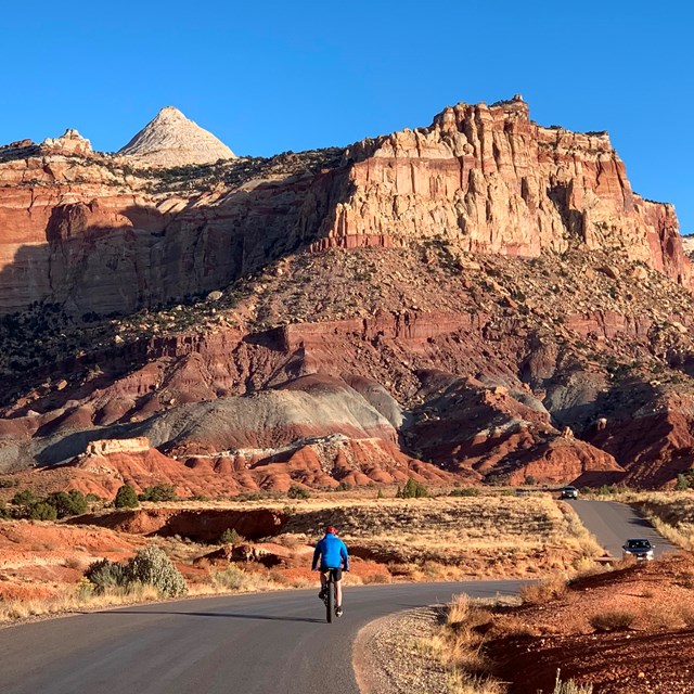 A bicyclist on a road next to tall cliffs