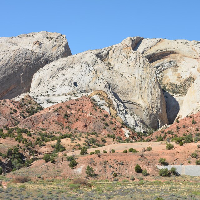 Blue sky, large white slopes, with red triangular shaped rocks below, green grass in the foreground