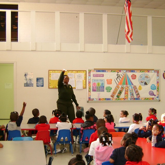Park ranger stands before classroom, before young students. 