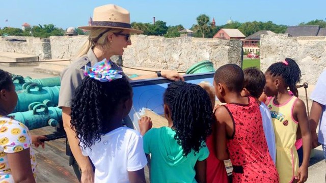 Ranger with a group of kids on gun deck by exhibit. 