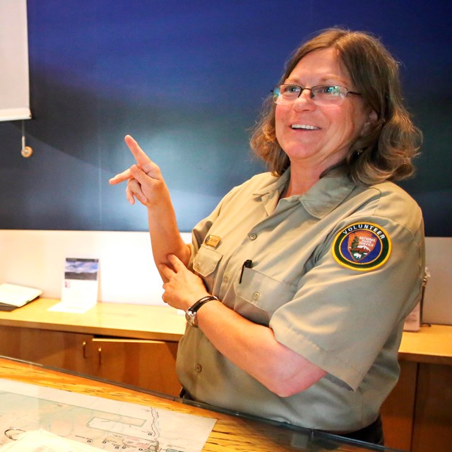 A person in an NPS volunteer uniform makes the letter K in American Sign Language with their hands.
