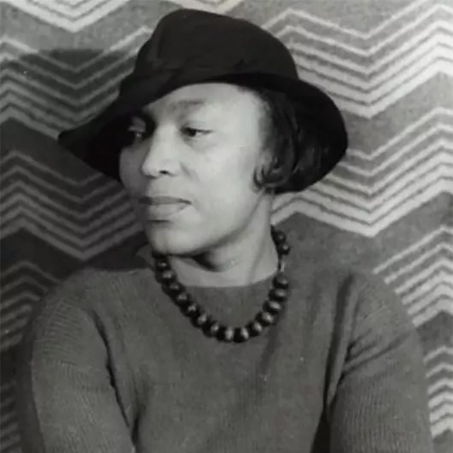 Head and shoulders portrait of an African American woman in a black hat and beaded necklace