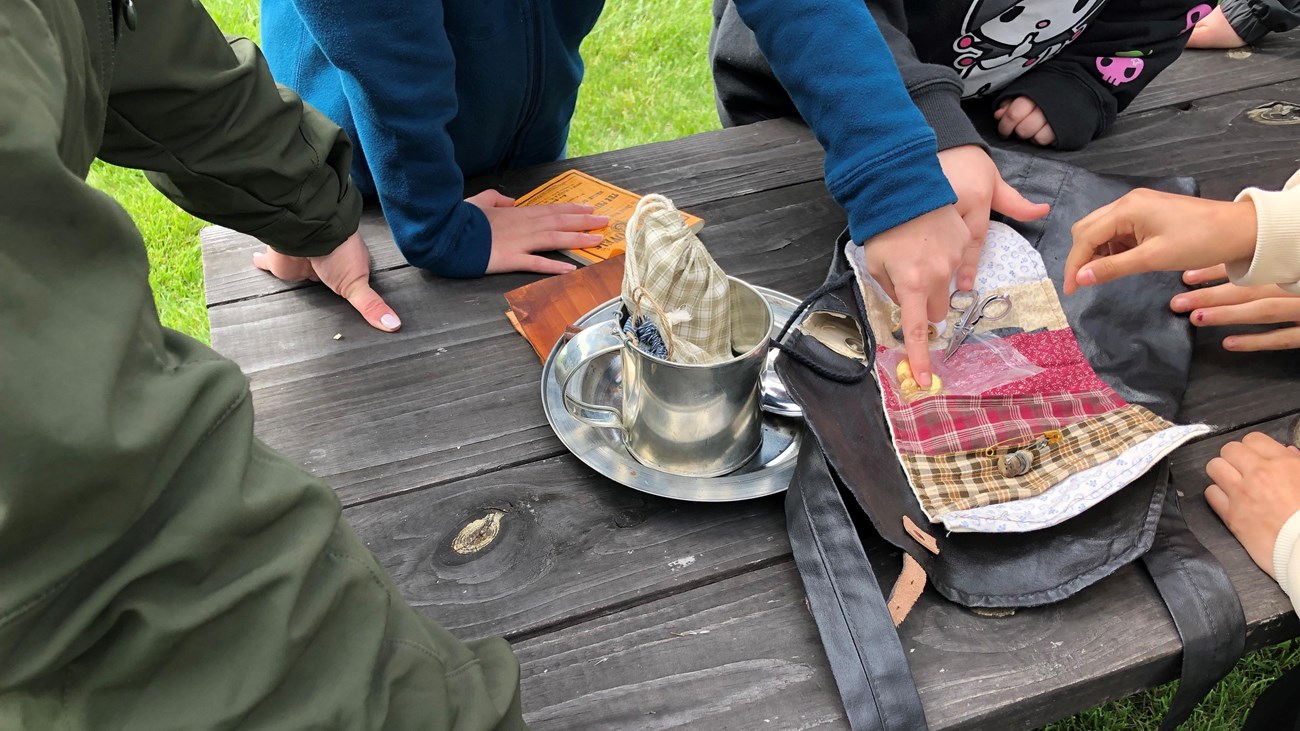 Children's hands explore replica artifacts of soldiers' belongings. 