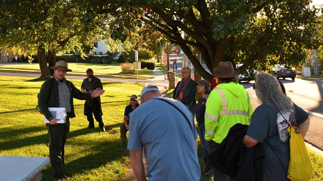 National Park Service ranger talks to a group of visitors under a large tree. 