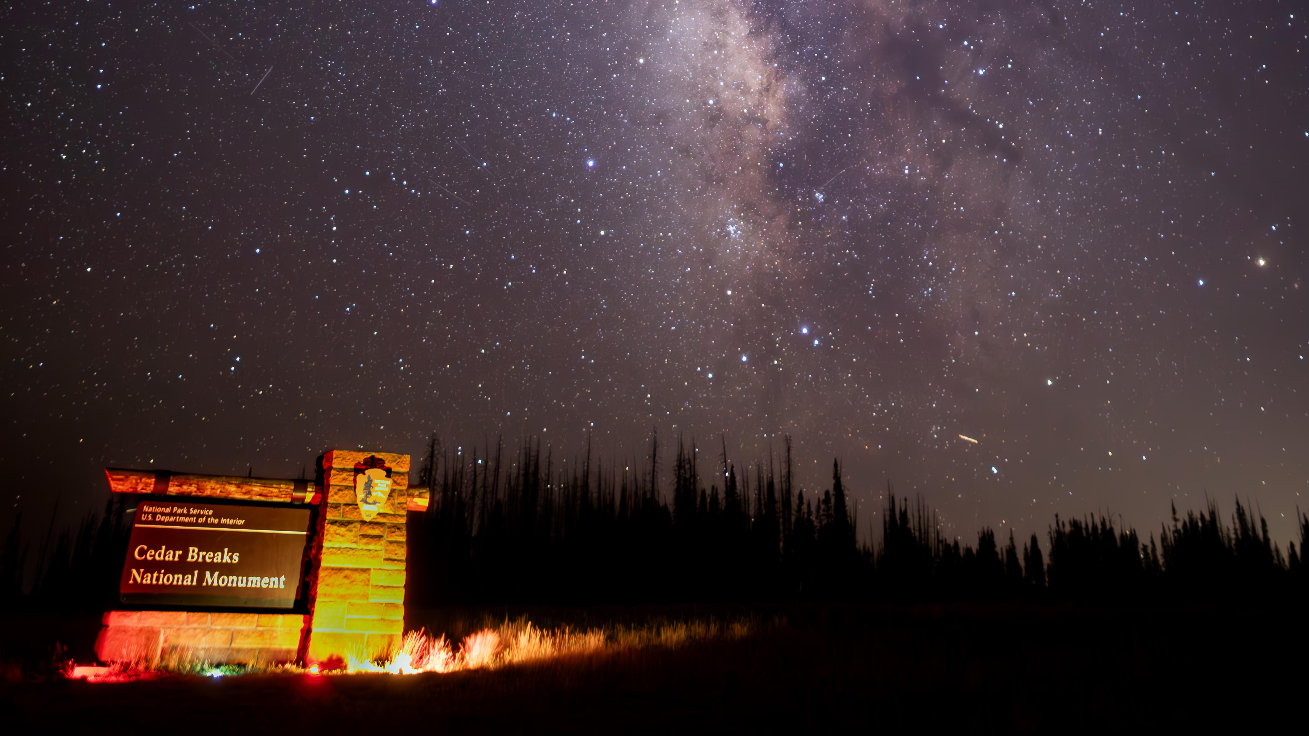 The Milky Way stretches across a star-filled night sky above the Cedar Breaks entry sign.
