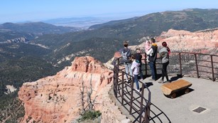 Several people stand at a railing overlooking the Cedar Breaks Amphitheater.