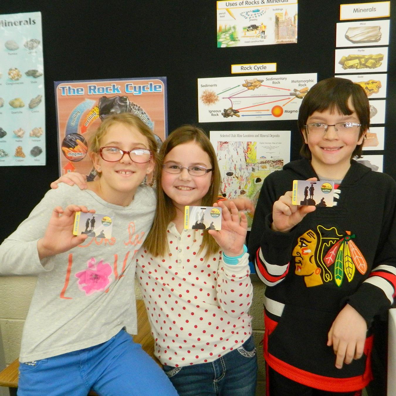 Three kids displaying their fourth grade park pass. 