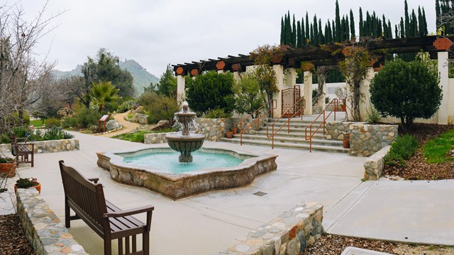 A fountain stands in the middle of a courtyard and garden.