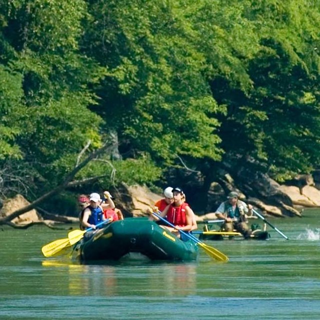 A photograph of a flotilla of rafts, kayak, and canoe on the river.