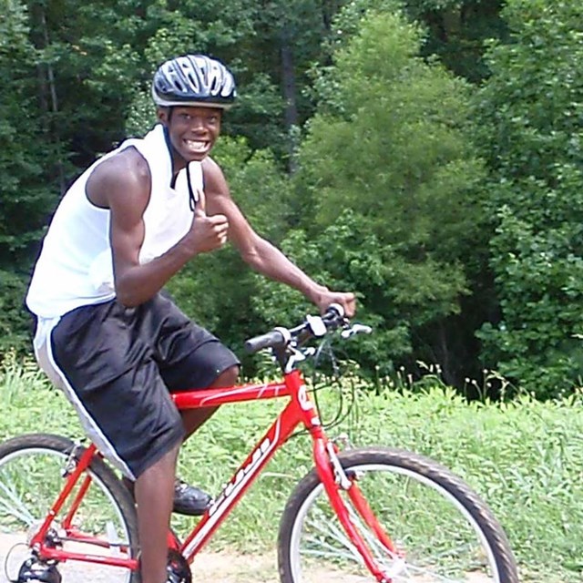Photograph of a cyclist giving a thumbs-up while riding on of the trails in the park.