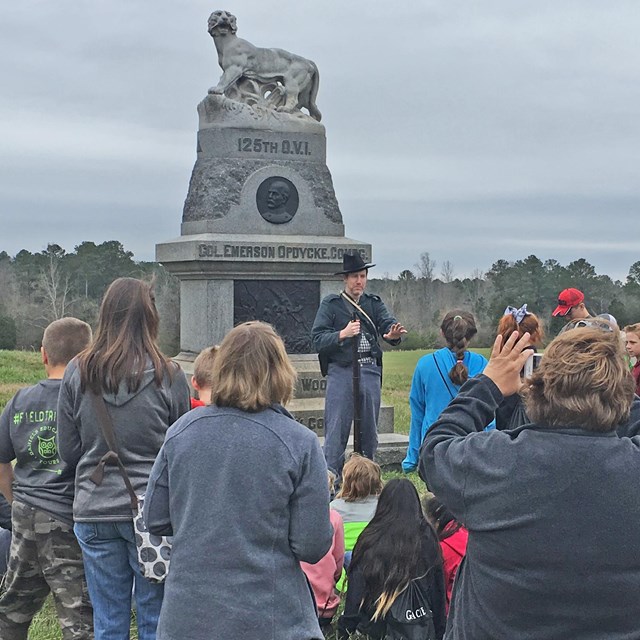 A man dressed in Civil War uniform talks to students in front of a monument