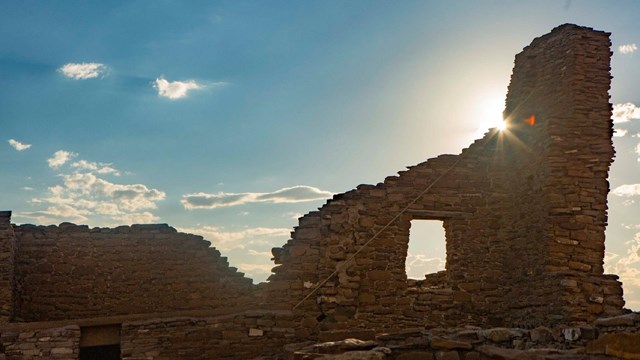 An upright sandstone wall and the sun shining behind it.