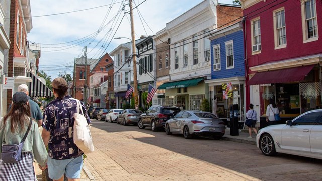 Two people walk along the sidewalk of a historic street in the mid-Atlantic.