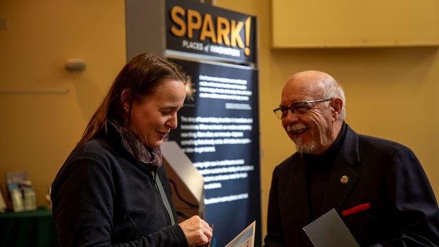 Two individuals engaged in conversation at an event with 'SPARK! Places of Innovation' banner.