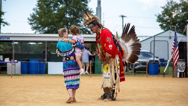 A woman holds a child while talking to a man in a dirt performance area