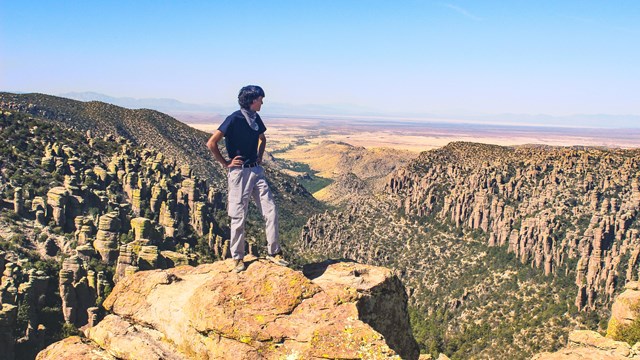 hiker standing on top of rock facing away toward valley of pinnacle rocks