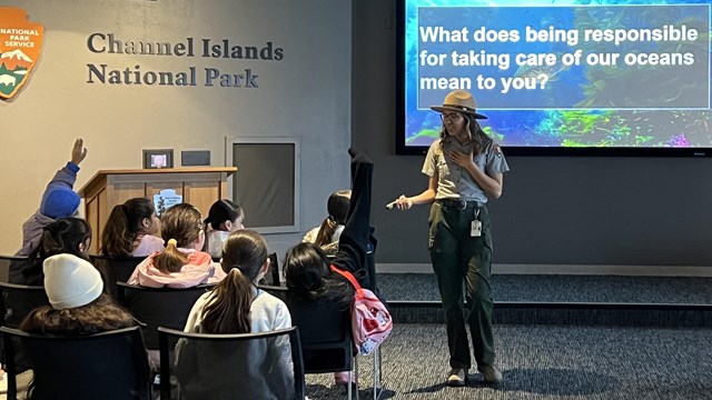 A ranger stands in front of a group of sitting students in a theater.