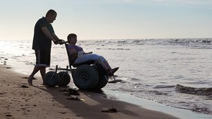 visitors on beach. one in wheelchair and the other pushing wheelchair. 