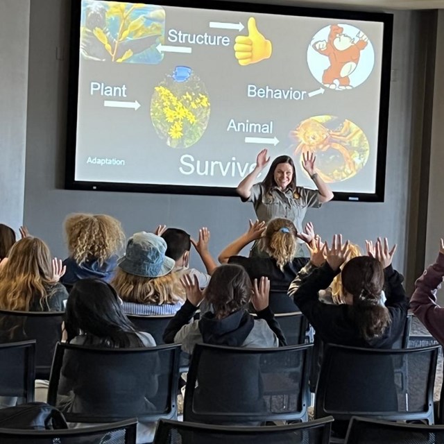 ranger with students in a theater with a slide show on the background screen