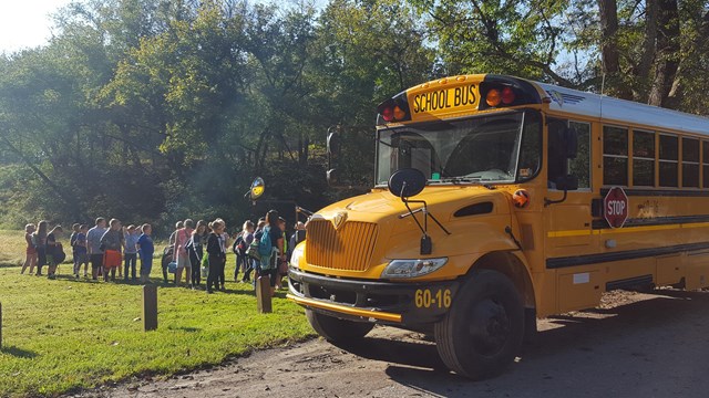 Students in line waiting to get on a yellow school bus.