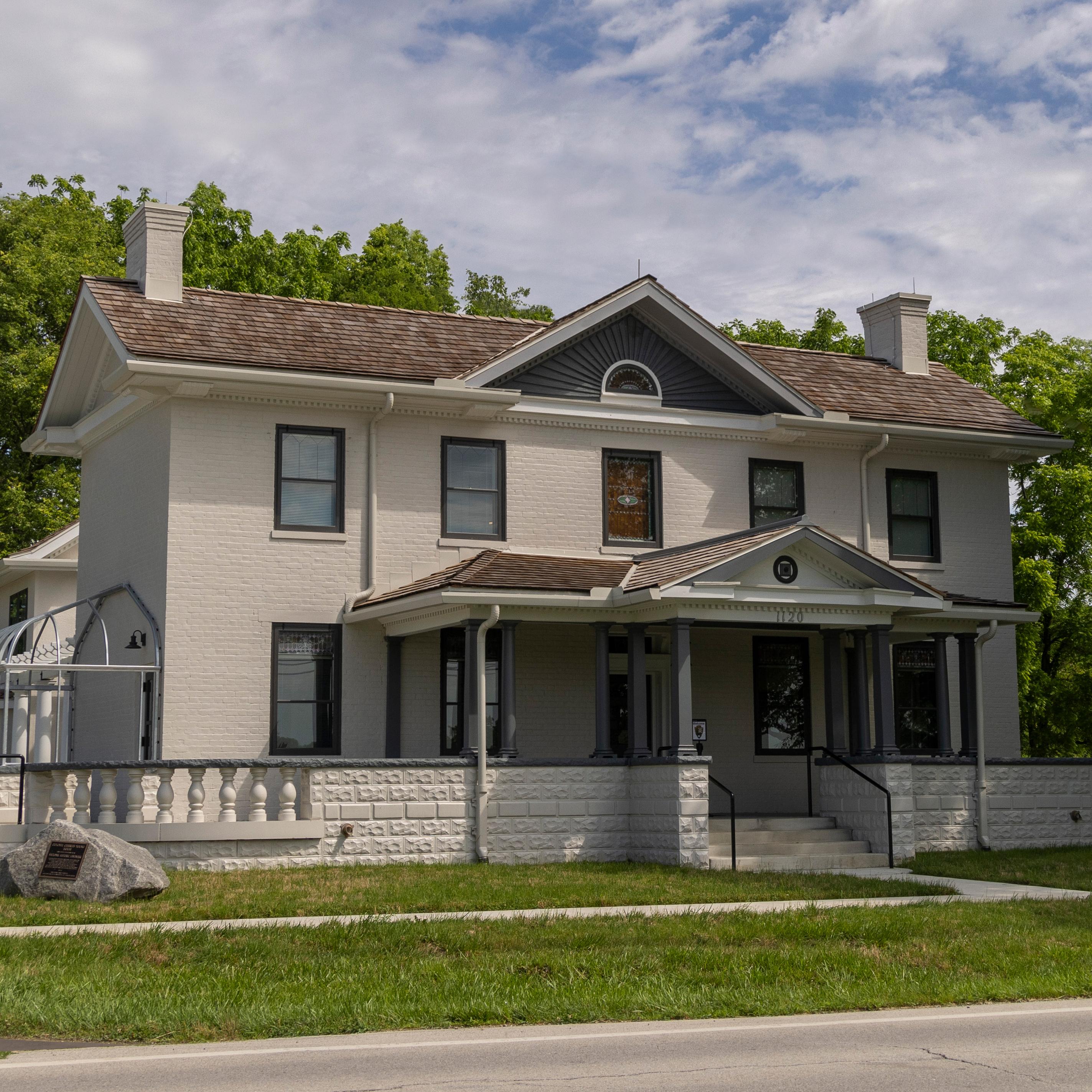 A large two-story house with five windows in a row on each level and a peaked roof in center.