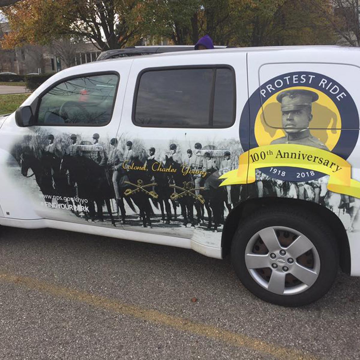 A car with wrapped artwork showing several mounted soldiers and portrait of Charles Young in circle